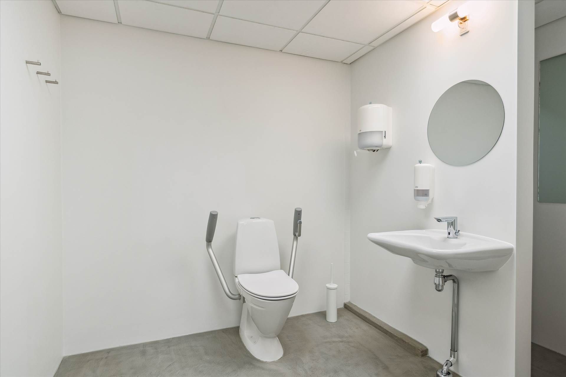 Et lille, hvidt badeværelse med højloft. Højloftet er hvidt og dækket af loftsplader. Et toilet med håndtag og en hvid,