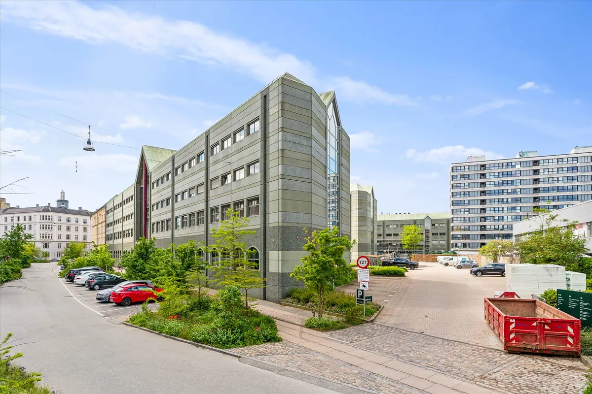 En bygning med flere parkerede biler og kontorer samt en stor rødt container til affald