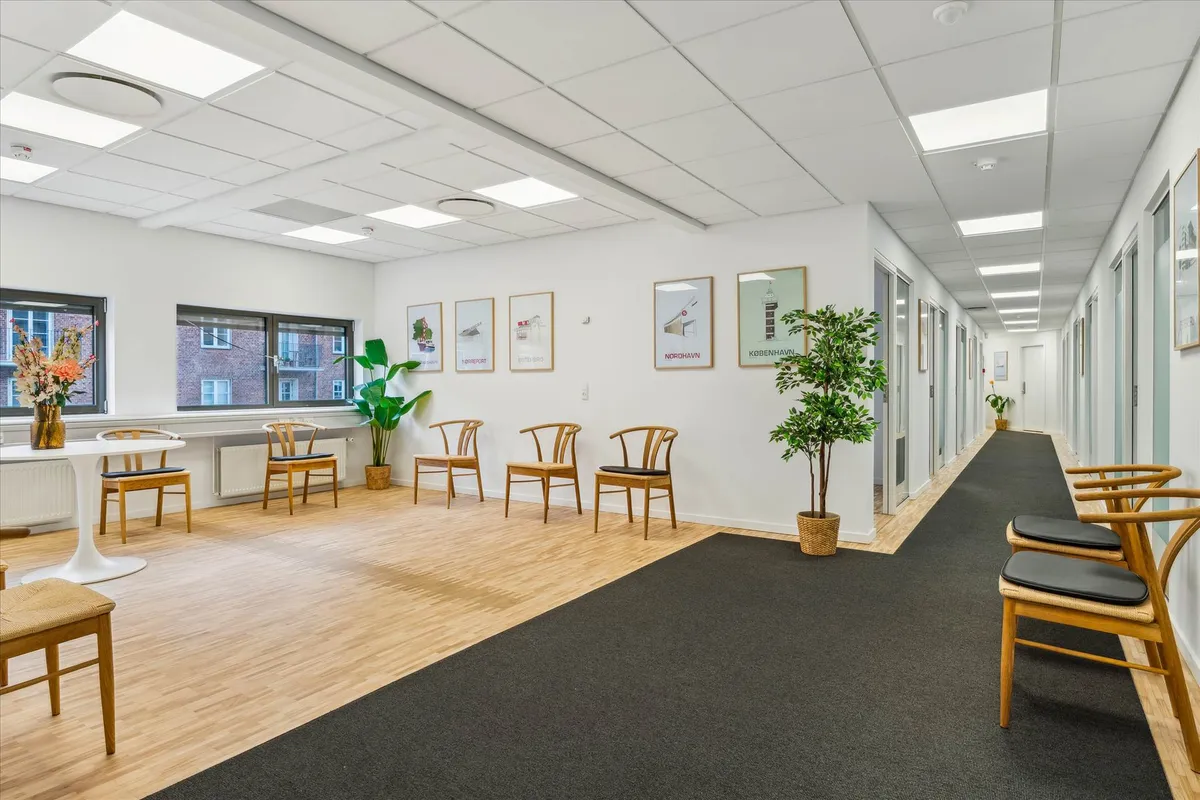 Inde i et sundhedscenter ses et lyse og luftigt værelse med lysegrå vægge og trægulve. På gulvet er der to længdeformede