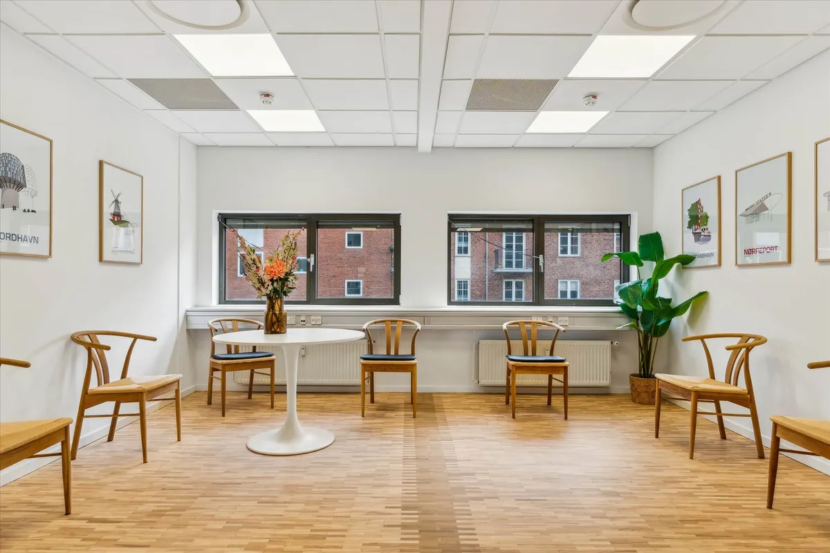 Minimalistisk kontorlokal med højt til loftet, hvidt loft og gulv, vinduer med udsigt til bygninger og planter