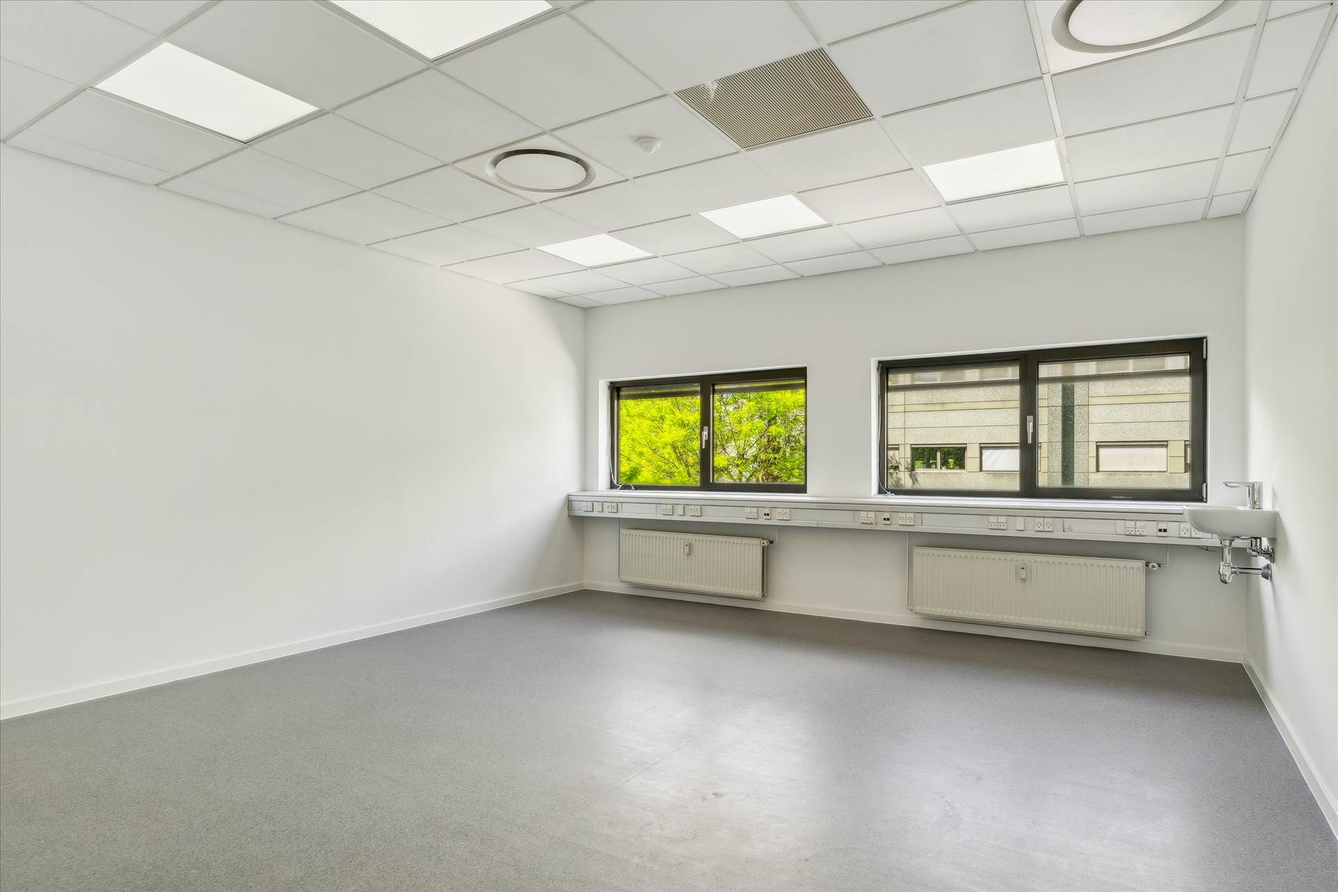 Remme med hvide vægge og gulv, to store ruder, hvide radiatorer, udstyrskonsol og lysekroner i loftet