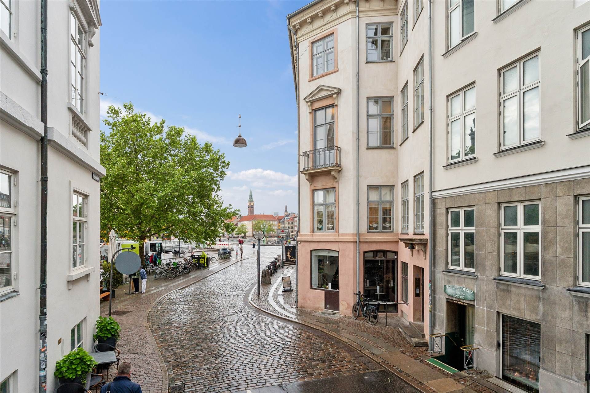 En smal vej med middelalderlige bygninger og stenbrolægning, med en gade med parkerede cykler og en person, der går i