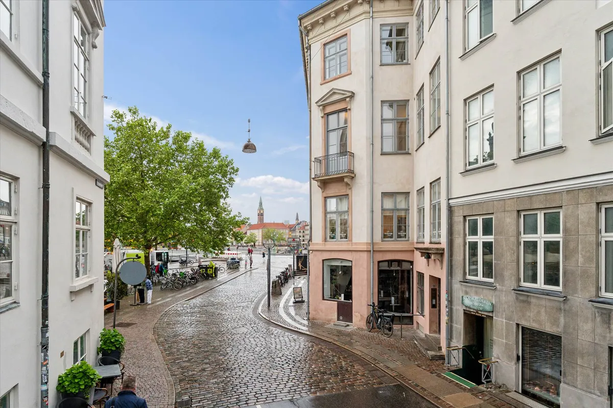 En smal vej med middelalderlige bygninger og stenbrolægning, med en gade med parkerede cykler og en person, der går i