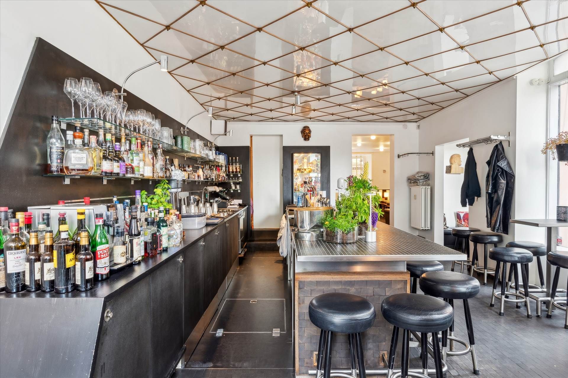 En elegant bar med sort marmordisk, høj hylde med glas og flasker, og smukt møbleret med læderstole og metalstole