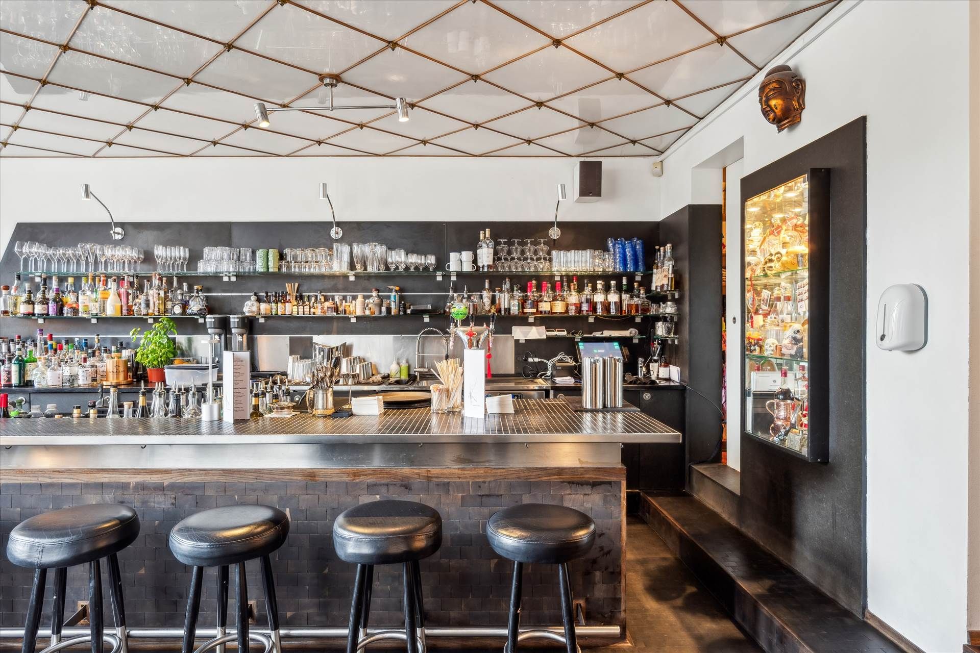 En moderne bar med høje stole, udskårne bardiske og et stort udvalg af drikkevarer og glas