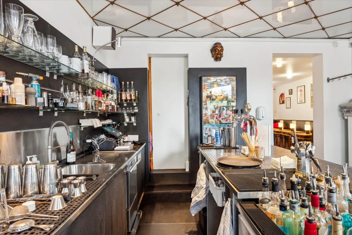 Glas og flasker på hylder, en åben dør, et spejl, et glasvæg og en maskine på en bar i et lokale