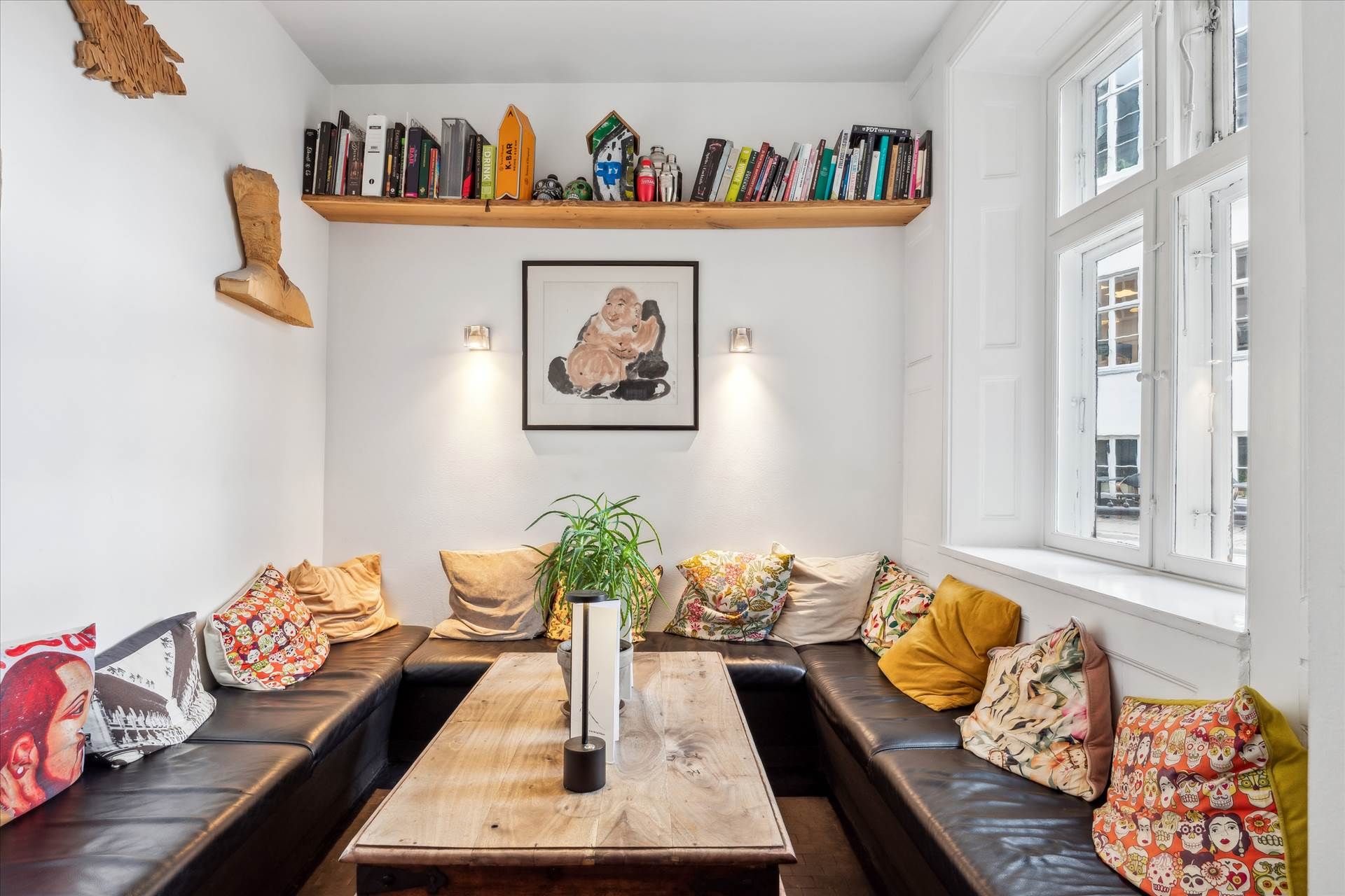 Lejlighed med lyse vindue, sofaer og et bord med plante og lamper på en hvid væg