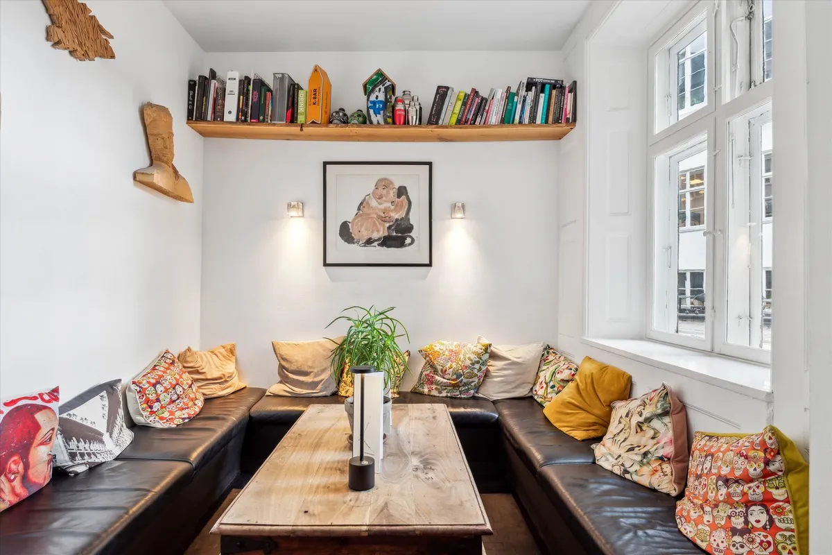 Lejlighed med lyse vindue, sofaer og et bord med plante og lamper på en hvid væg