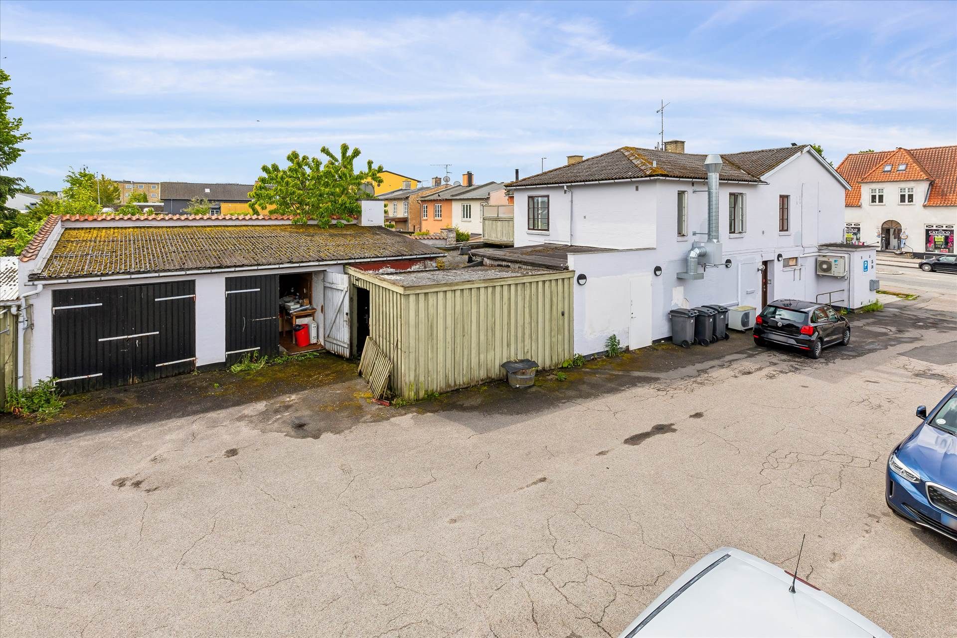 En tom parkeringsplads med to biler og garager samt en række huse og kontorer bagved