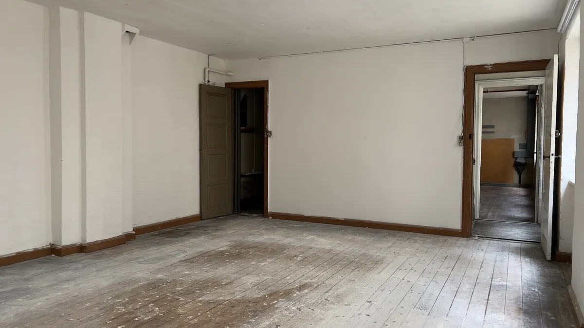 En tom og ren stue med åbne døre til siden og gulvet og væggene er træfarvede og har nye hvide malingsspor.