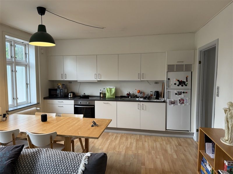 Et moderne køkken med hvide skabe og en træbord med stole samt en hvid køleskab med magneter og en statue på hylden