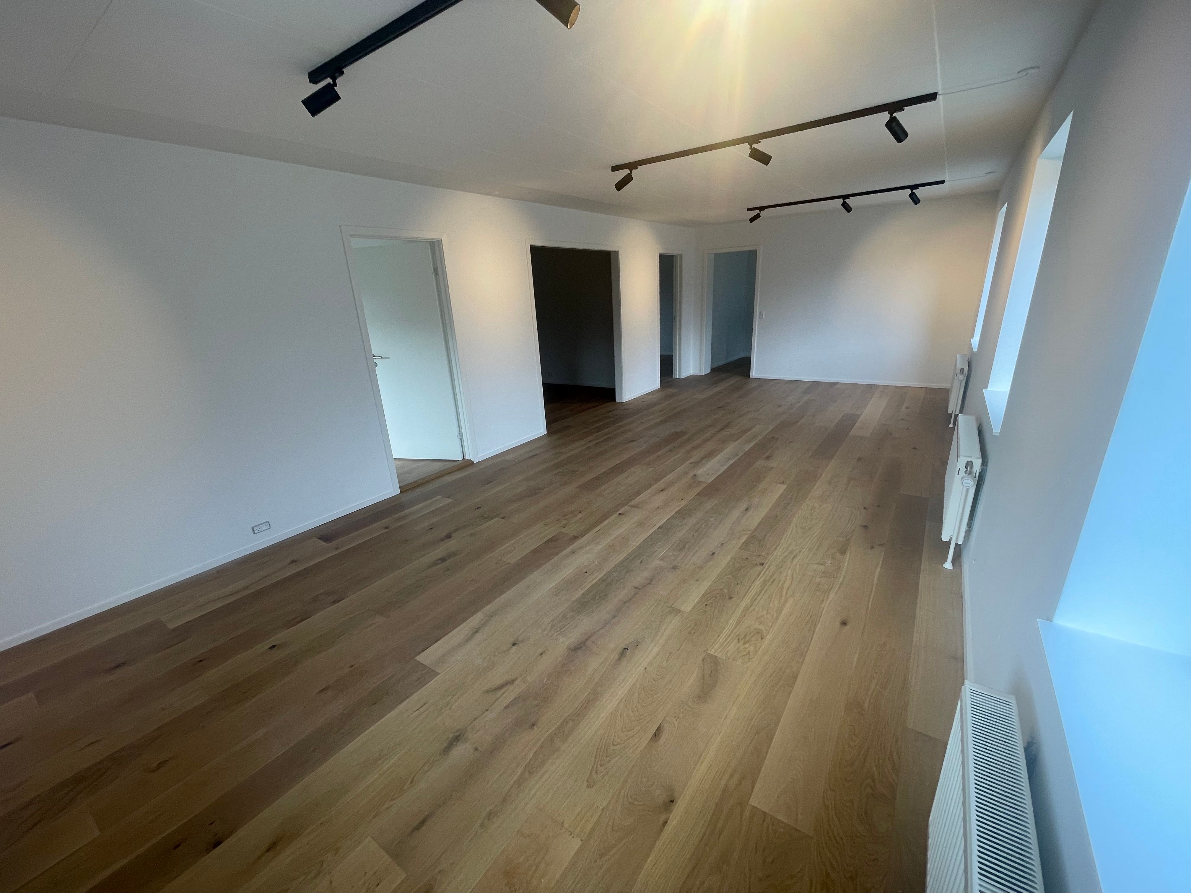 Et nyt kontor med massivt trægulv, lyse hvide vægge, store vinduer, og lysepunkter på loftet