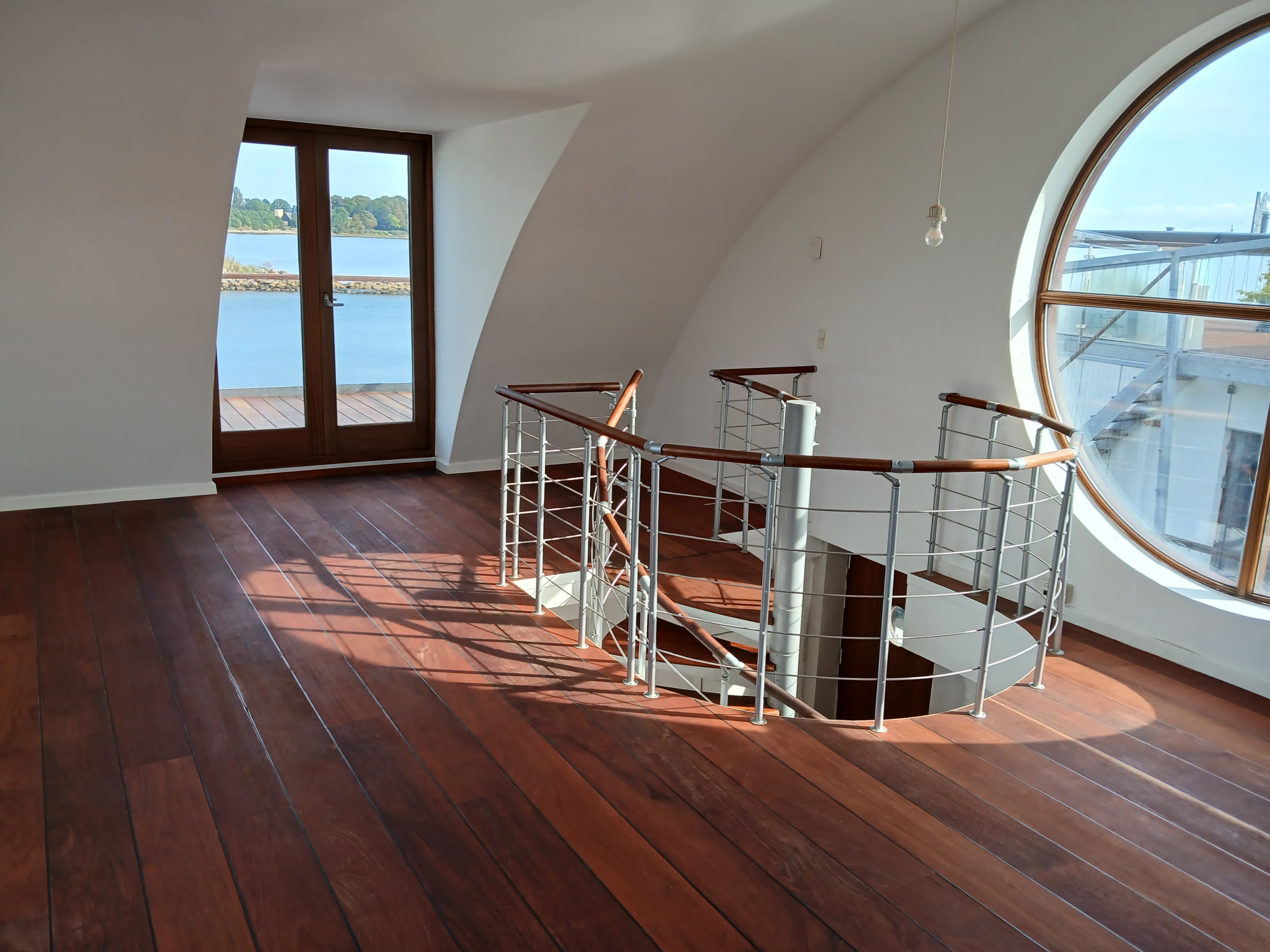 Nyrenoveret husbåd med moderne udsmykning, hvidt loft, spiraltrappe og udendørs terrasse med udsigt over vandet og grønne