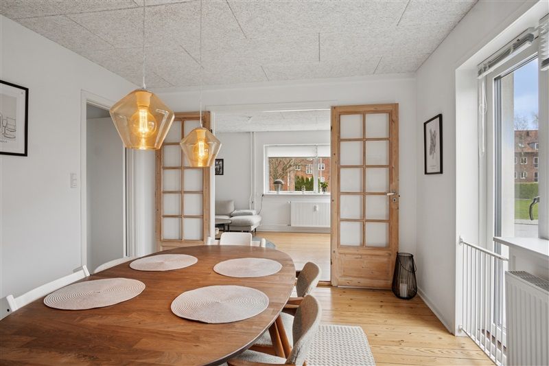 Moderne lyse stue med lyse pletter og lyse gulvbelægning med en træbord og stole samt en sofa og plante i baggrunden