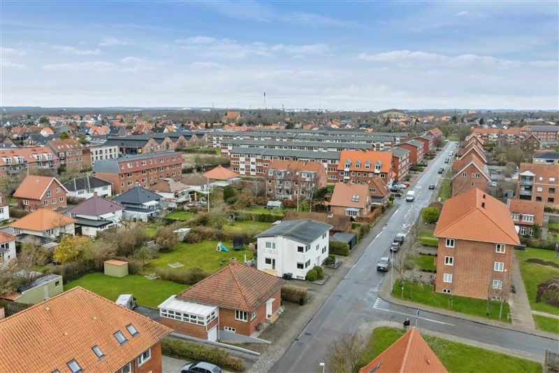 Kvarter med rækkehuse og parcelhuse, lyse himmel, biler parkeret og grønne marker i forgrunden
