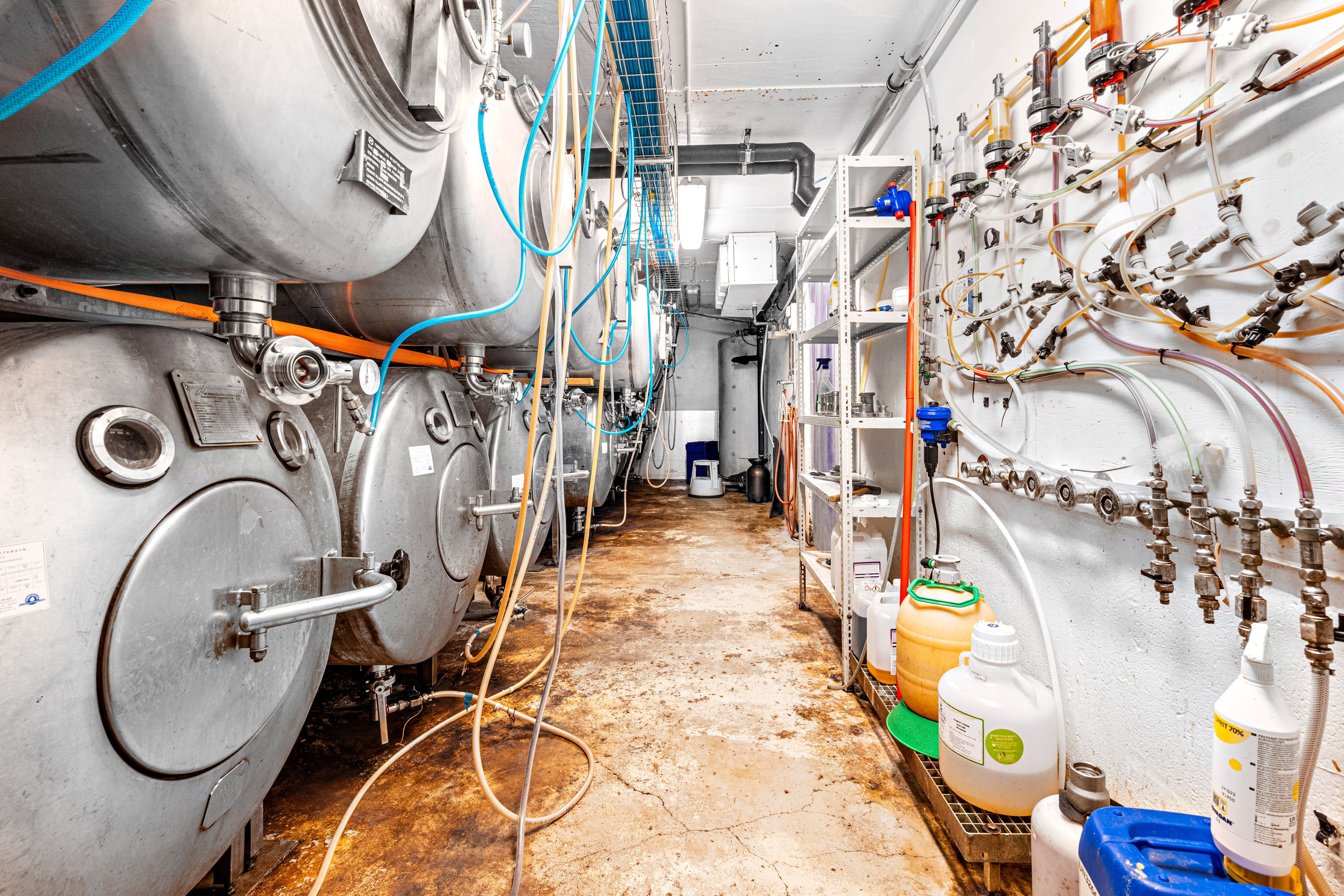 Inde i bryggeriet ser man store ståltanke med slangeforbindelser og rørsystemer, flasker og kegs samt rensningsudstyr for øl