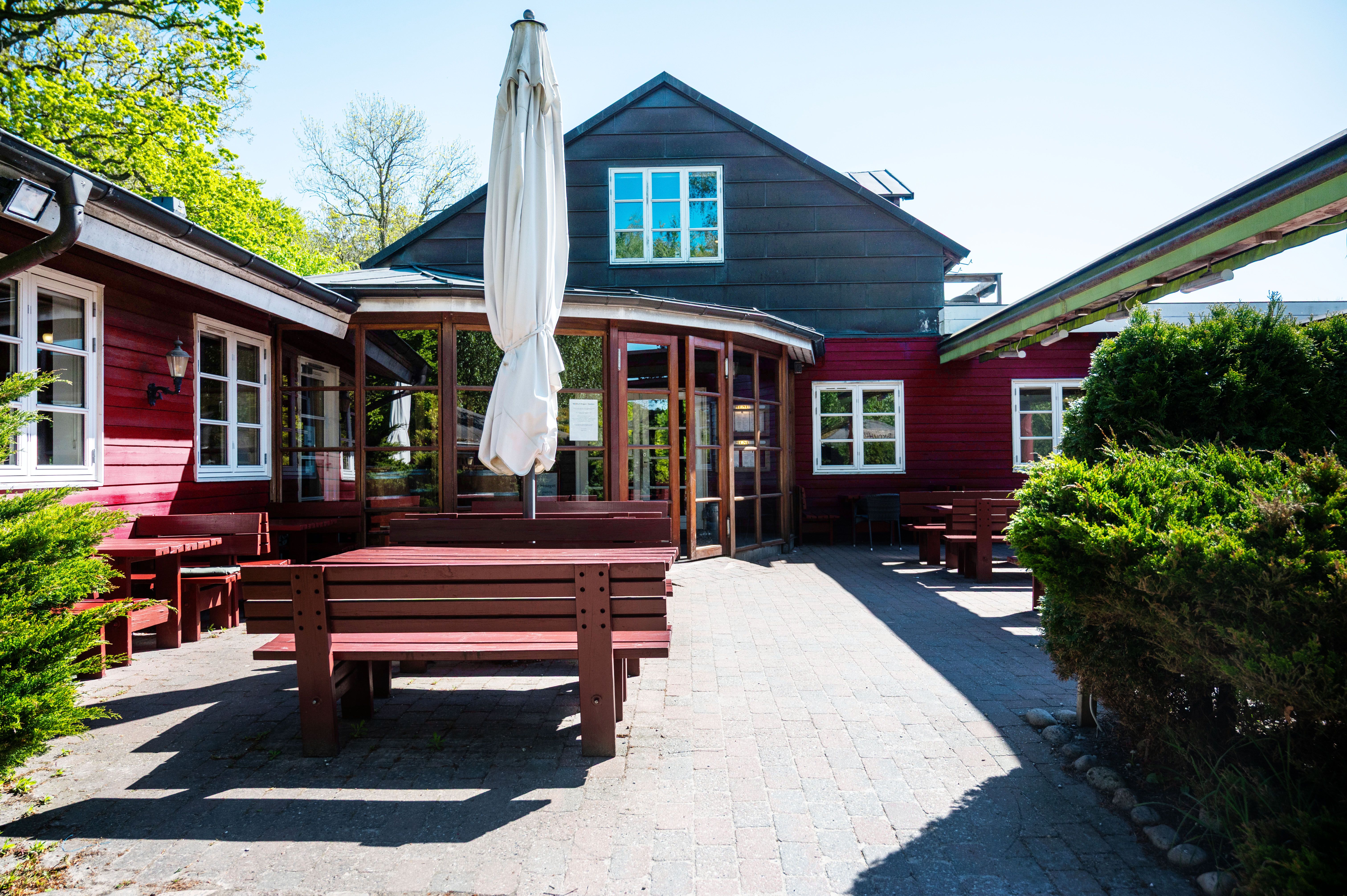 Rødt bygning med to terrasser, hvor den ene har åbne glasdøre og hvide parasoller