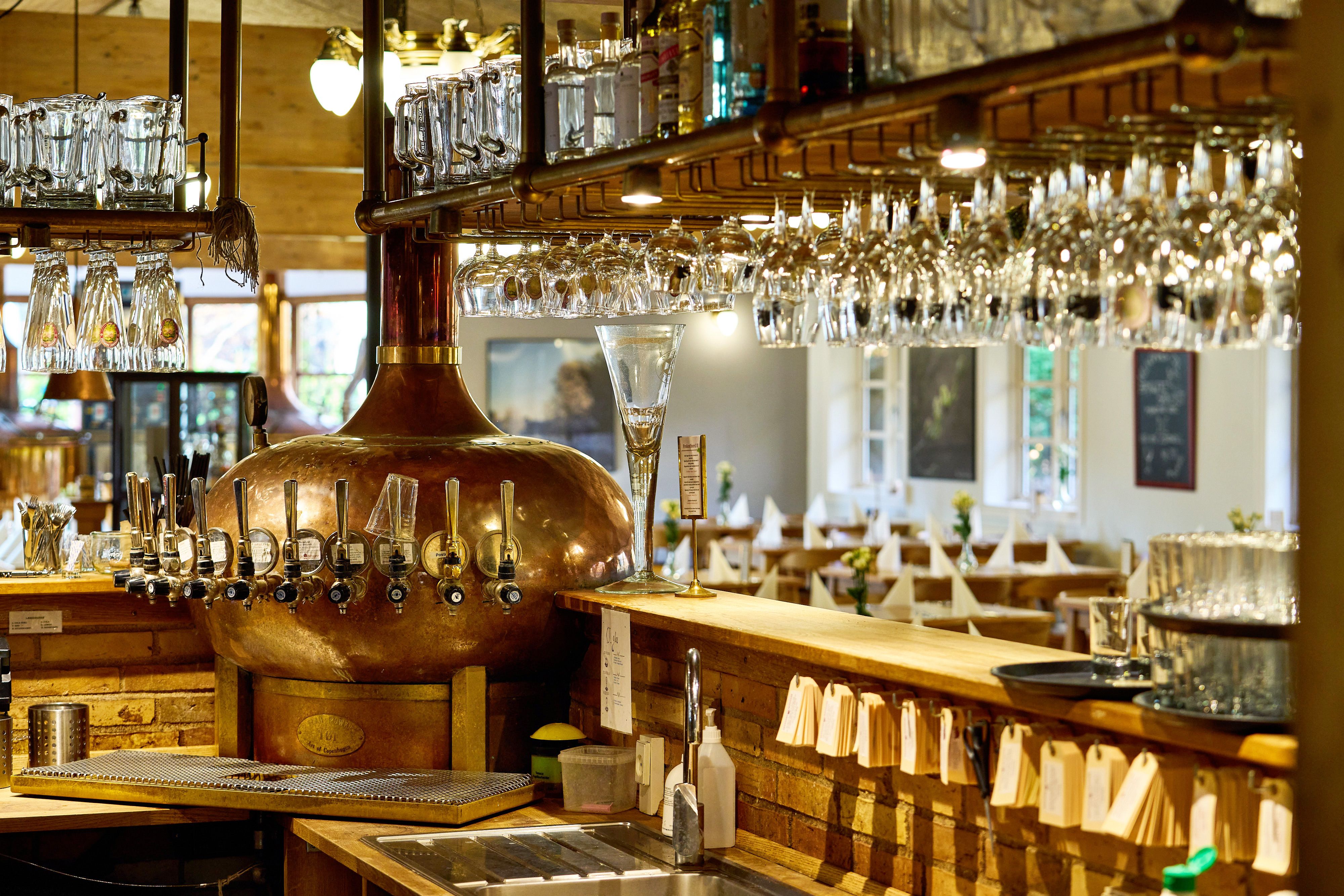 En stor rustfrit stål bræsestang med flasker og gläser i baren i et hyggeligt bryggeri og restaurant med smagfuldt interiør