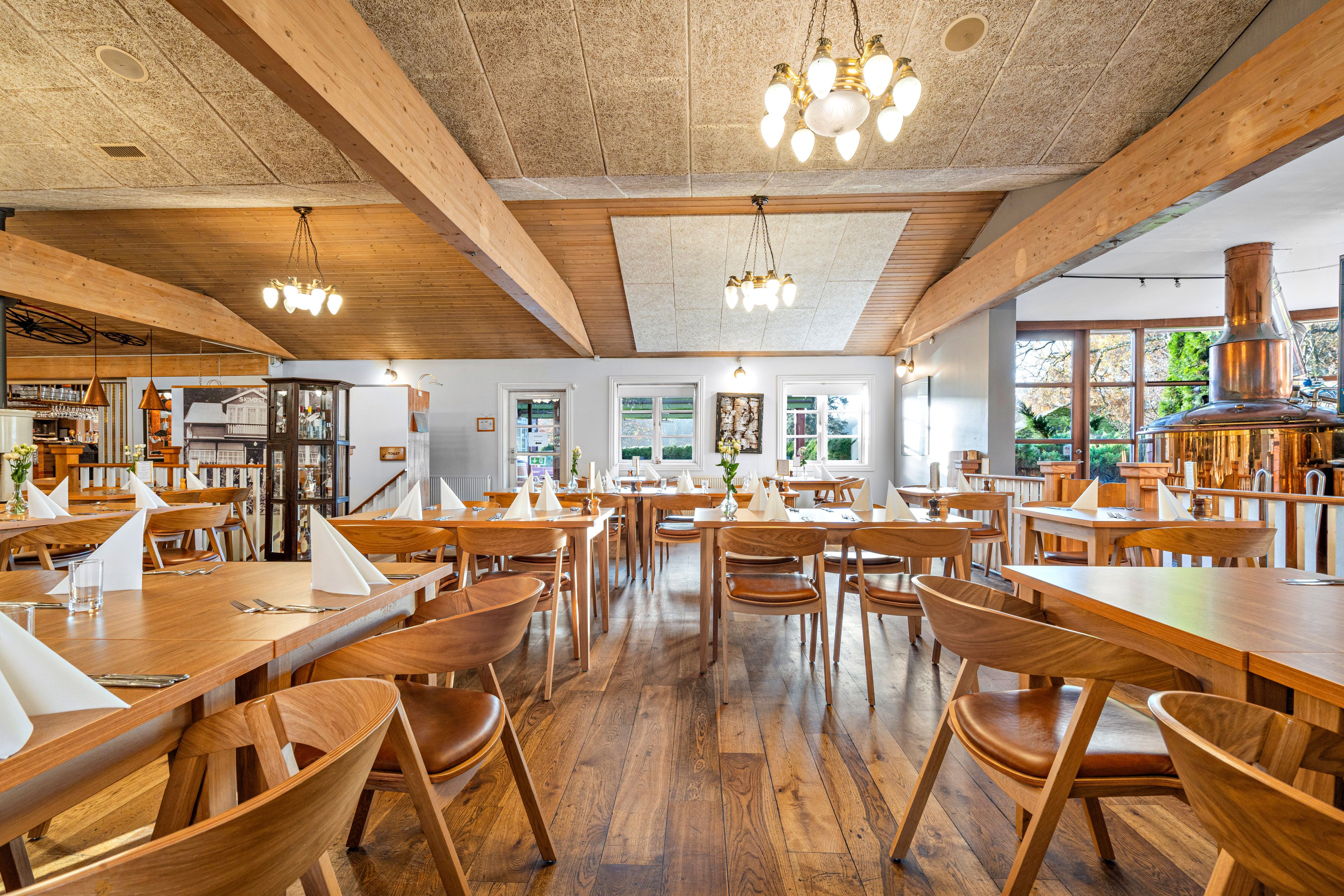 Restaurant med lyse loftsbjælker og trægulve. Rundt 150 gæster kan finde plads på selskabslokaler med lyse vinduer og