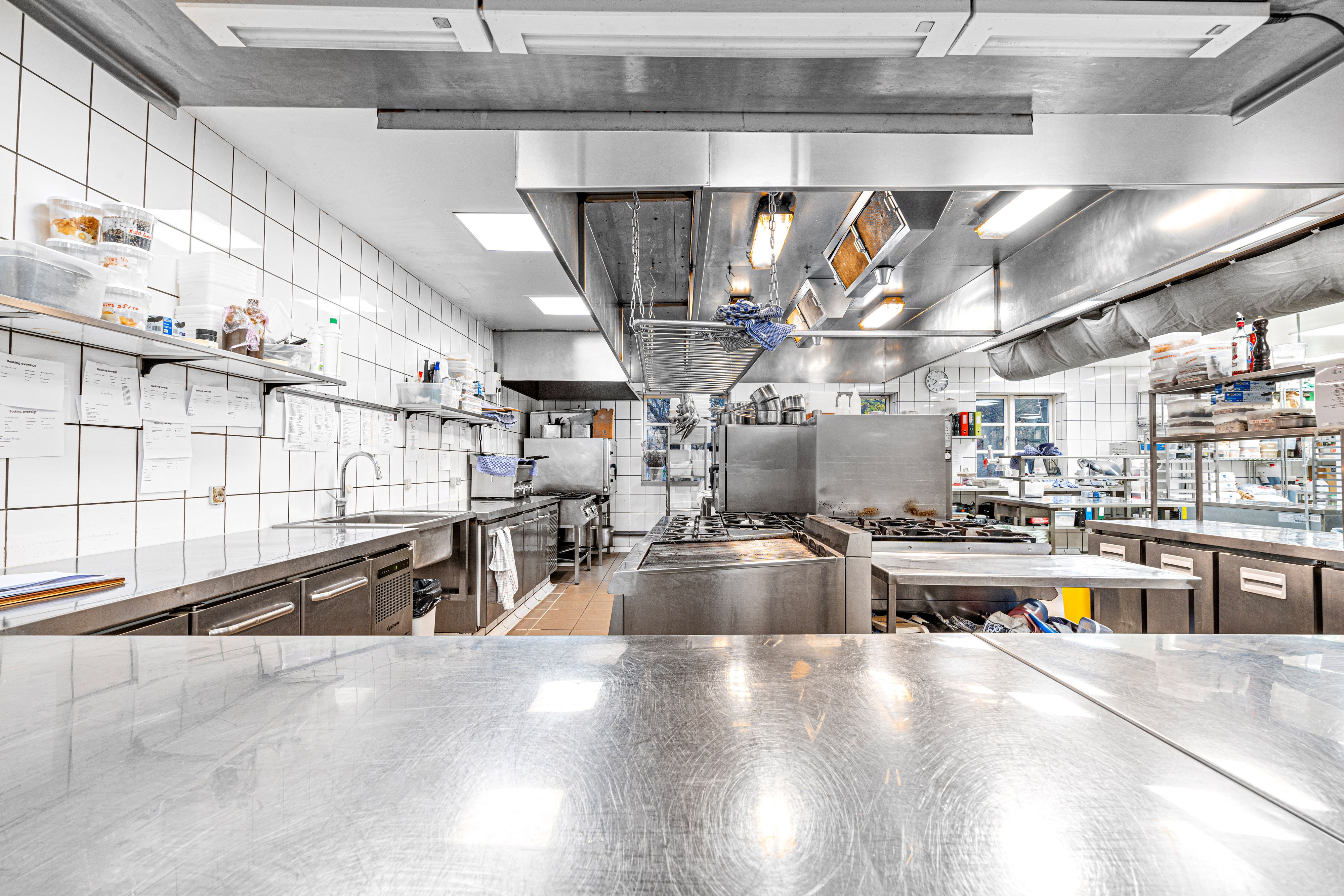 Et moderne kommercielt køkken med rustfrit stålborde, vægge og køleskabe samt store ovne og udstyr til madlavning