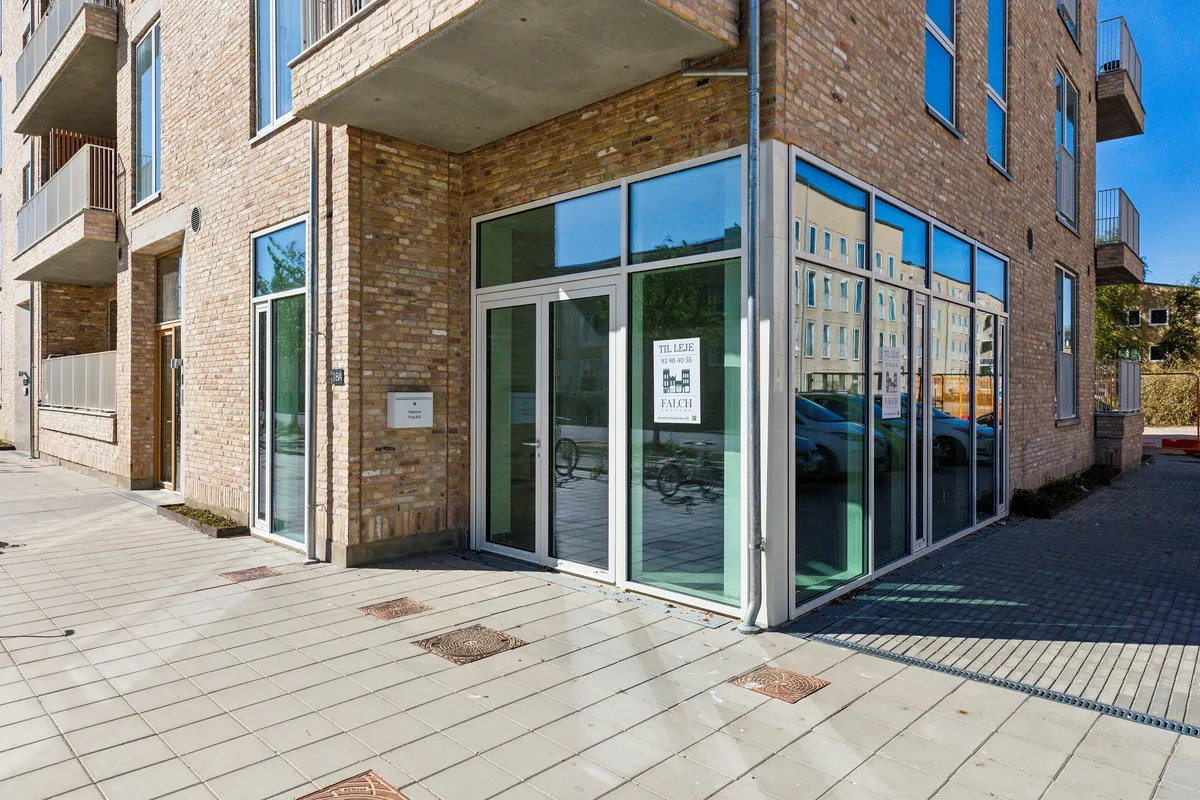 Lejlighedsbygning med glasdøre og spejle, facade ud mod gade, to biler reflekteret i spejlet, skilt med tekst og logo, biler