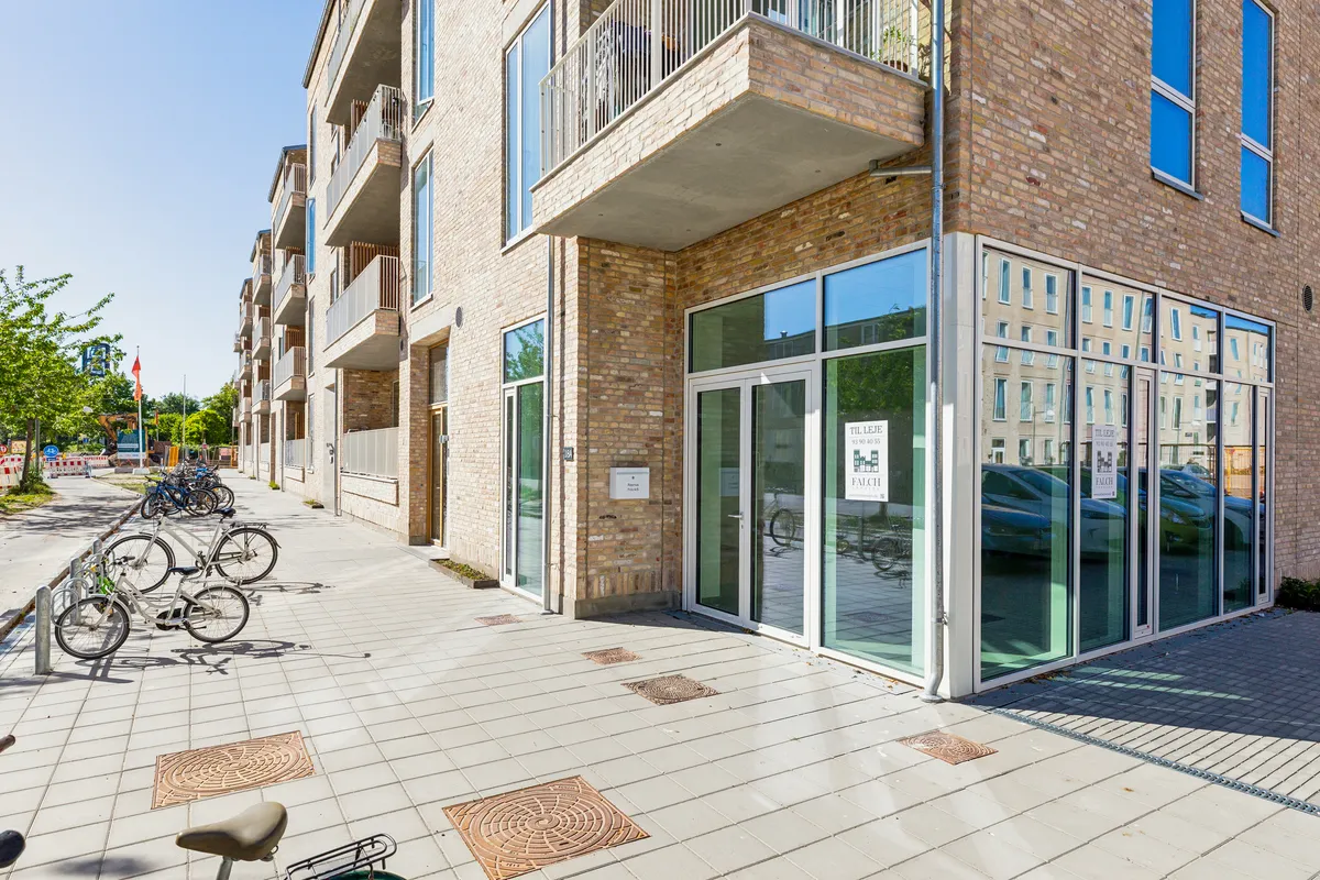 En hjørnebygning med glasdøre og vinduer samt parkerede cykler og et rødt flag på en stang