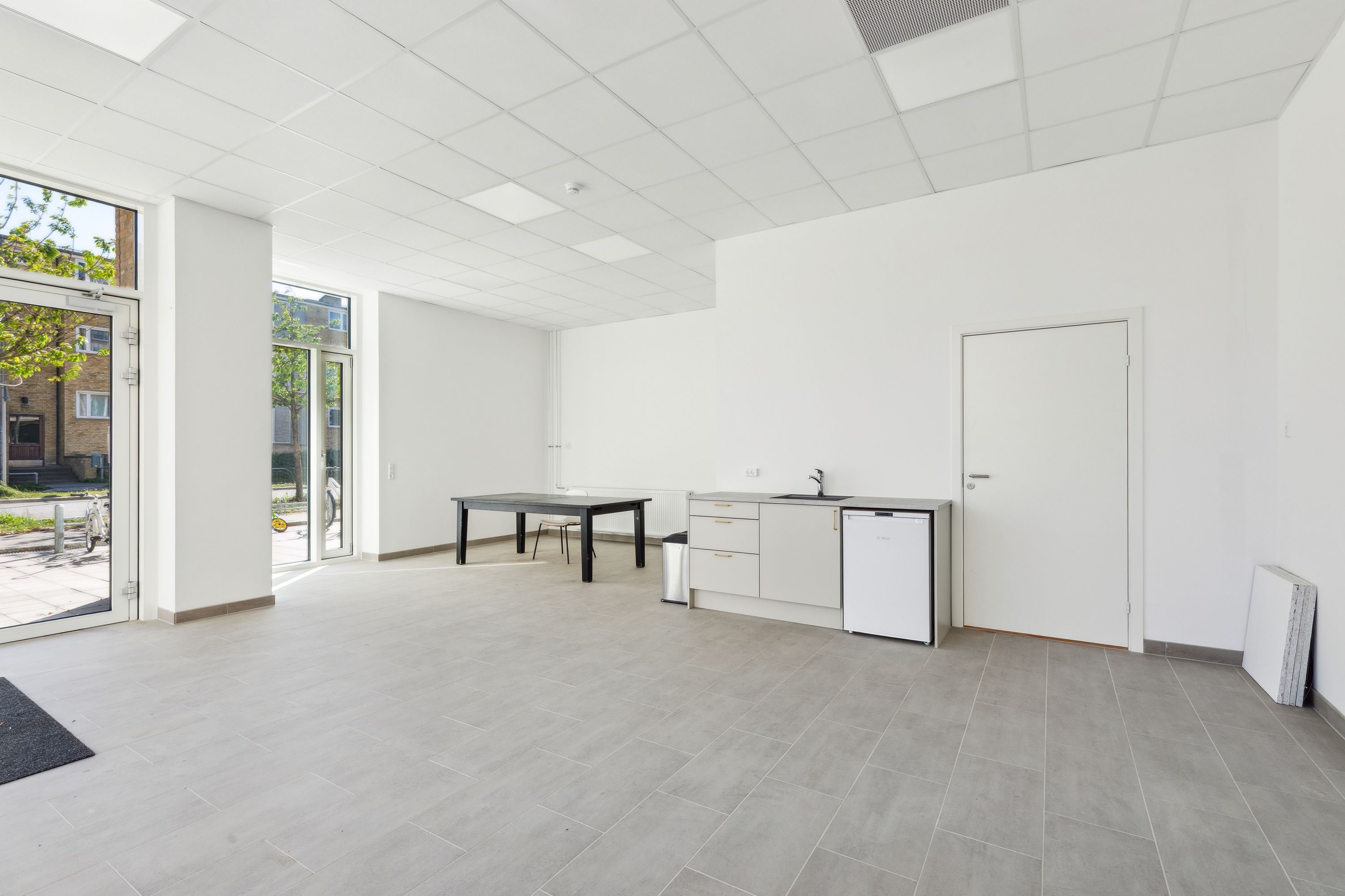 Store, lyse værelser med moderne møbler og trægulv. Et køkken med hvide vægge og møbler og en dør til et badeværelse. Et