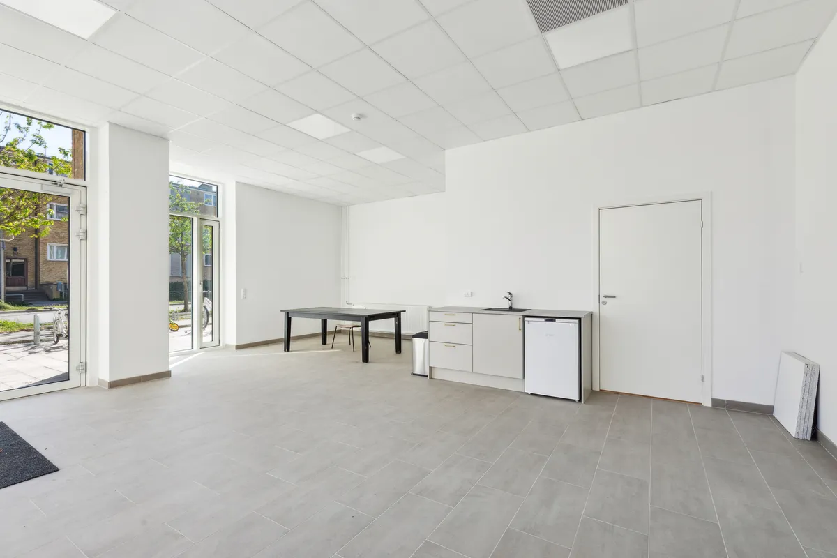 Store, lyse værelser med moderne møbler og trægulv. Et køkken med hvide vægge og møbler og en dør til et badeværelse. Et