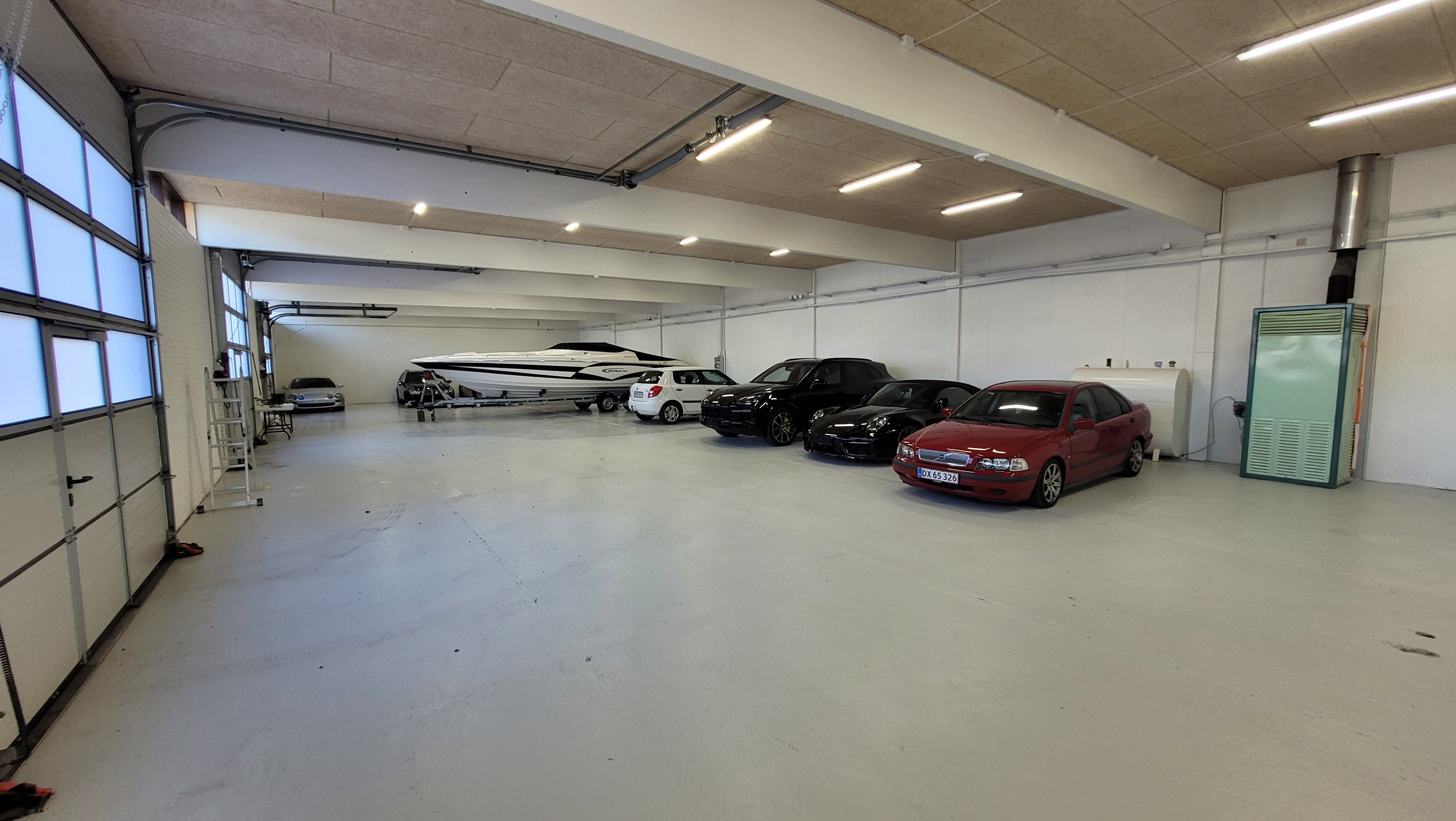 Et tomt lagerlokale med flere biler og en båd parkeret i garagen, en hvid metalle trappe og store vinduer foran
