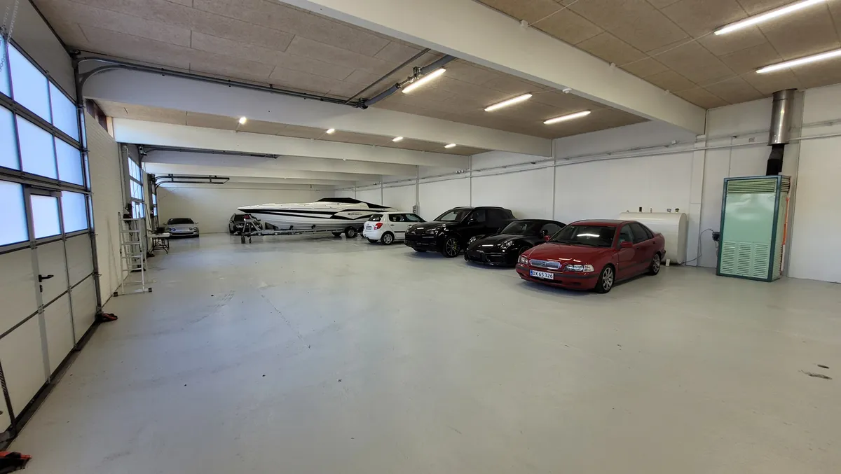 Et tomt lagerlokale med flere biler og en båd parkeret i garagen, en hvid metalle trappe og store vinduer foran