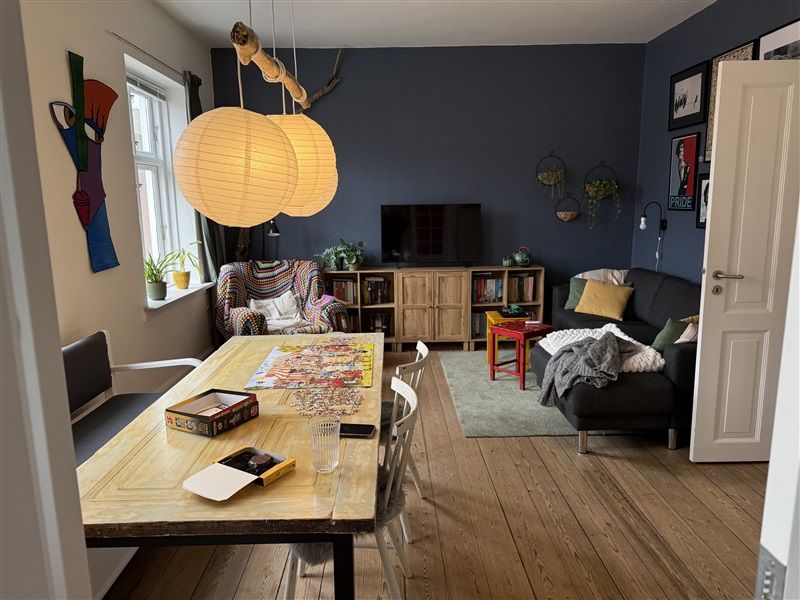 Lys stue med højt loft og gult bord, tv og sofa med puder og tæpper