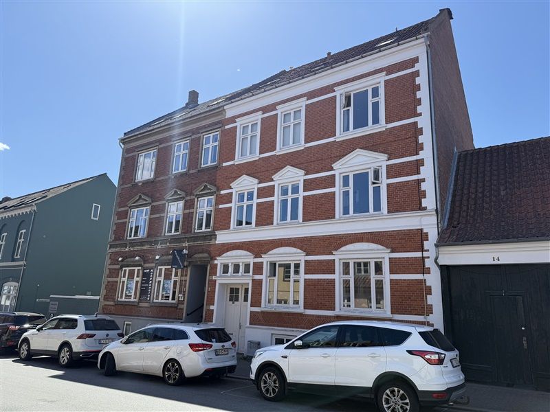 Tre hvide SUV-biler parkeret foran en stor bygning med røde mursten og hvide vindueskarme