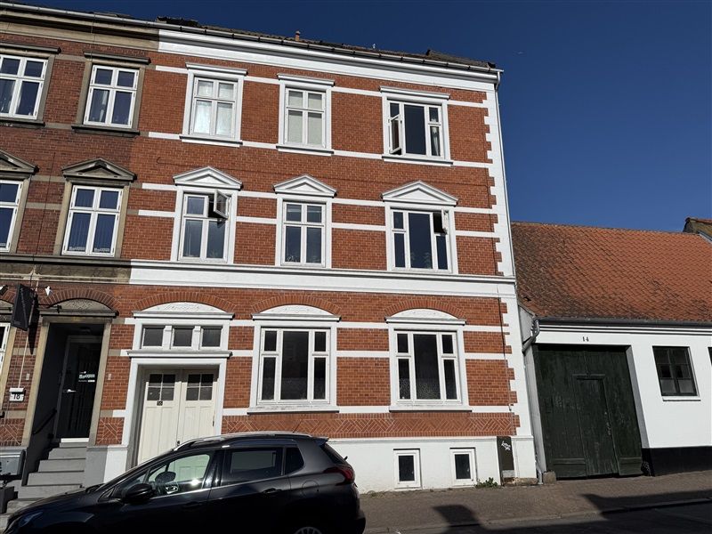 To-etages røde murstensbygning med hvide vinduer og døre samt grønne garageporte i Fredericia midtby