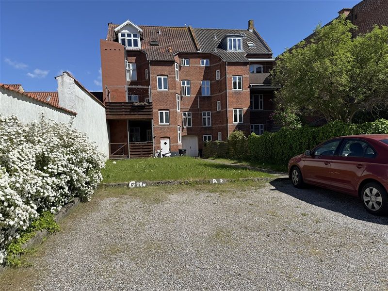 En parkeringsplads foran en bygning med røde mursten og hvide vinduerne i Fredericia