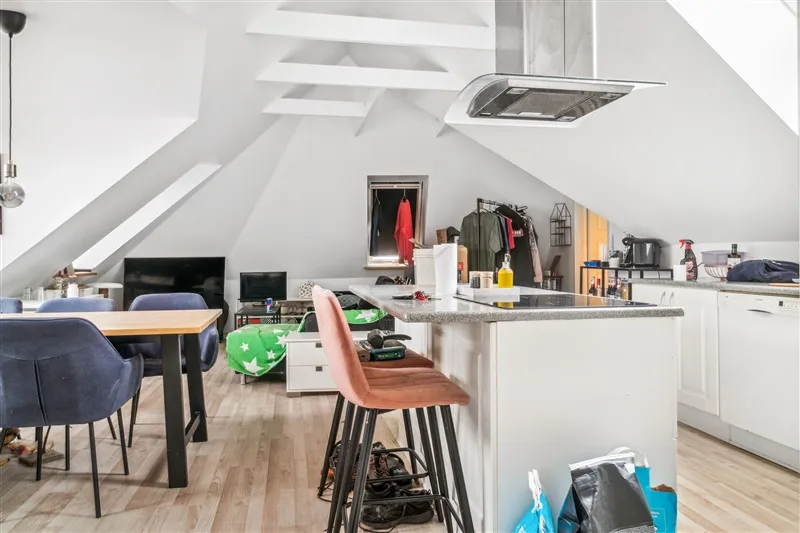 Loftslejlighed med loftsrum, højloft, køkken, spisebord og høje stole med trægulv og højloft med tøjvægge og garderobe