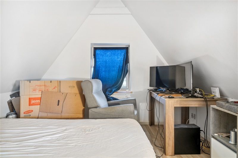 Et loftsværelse med en seng og et skrivebord med en monitor, en stol og flere kasser