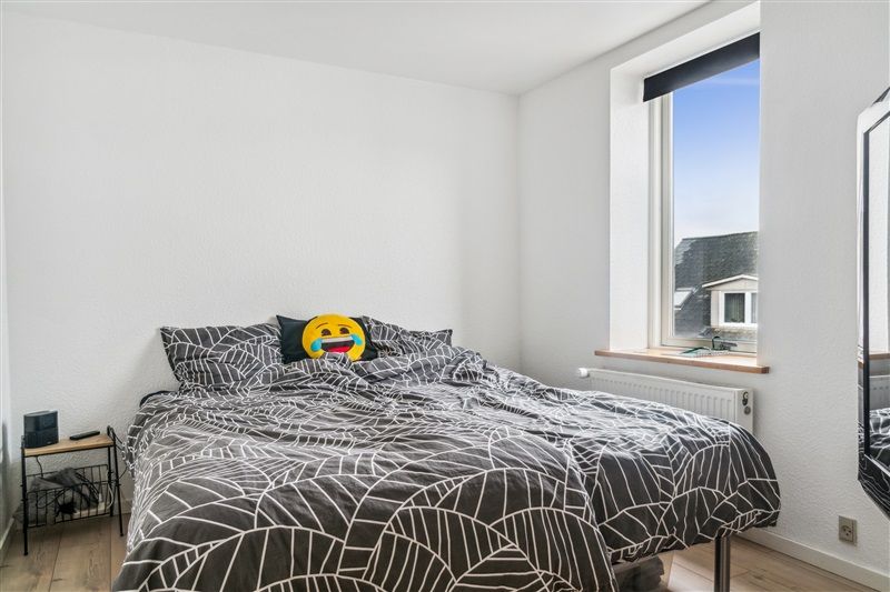 En soveværelse med et enkelt dobbeltseng, hvor der er en emojipude med et smilende ansigt og en sort højttaler på en lille