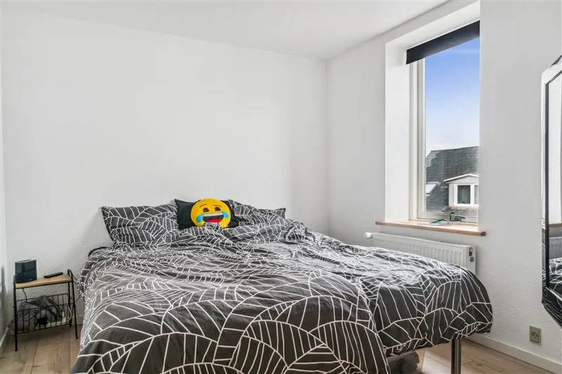 En soveværelse med et enkelt dobbeltseng, hvor der er en emojipude med et smilende ansigt og en sort højttaler på en lille