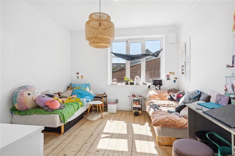 To værelser med lyse trægulve og hvide vægge med hængende lys og en stor vindue med udsigt til en bygning og en havvind.