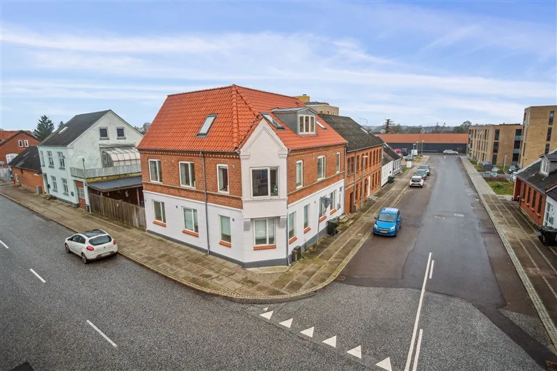 Bygning med rødt tag og mange vinduer med en parkeringsplads og biler foran