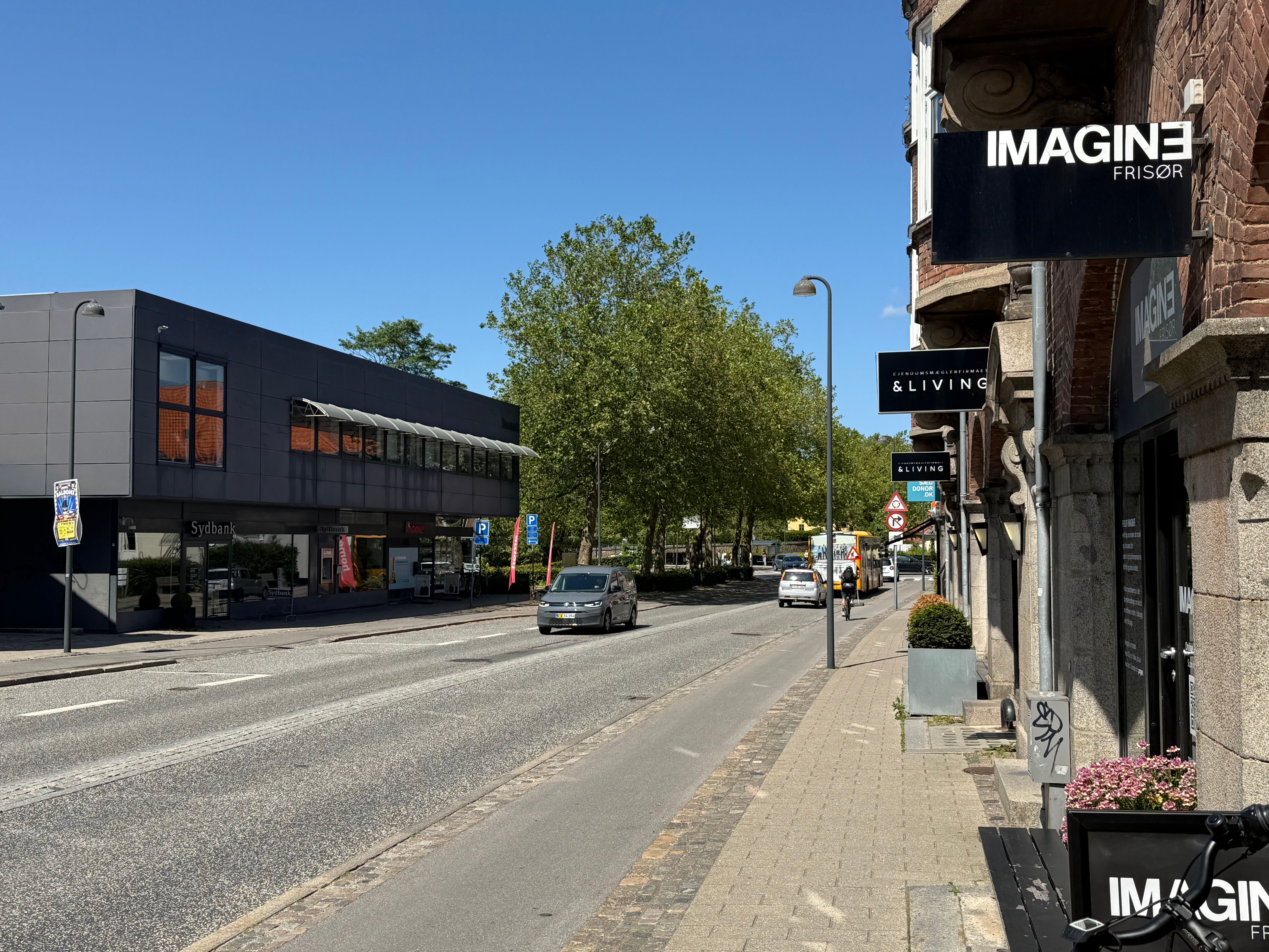 Lyngby Hovedgade med to biler og en cykel i forgrunden og en bus i baggrunden