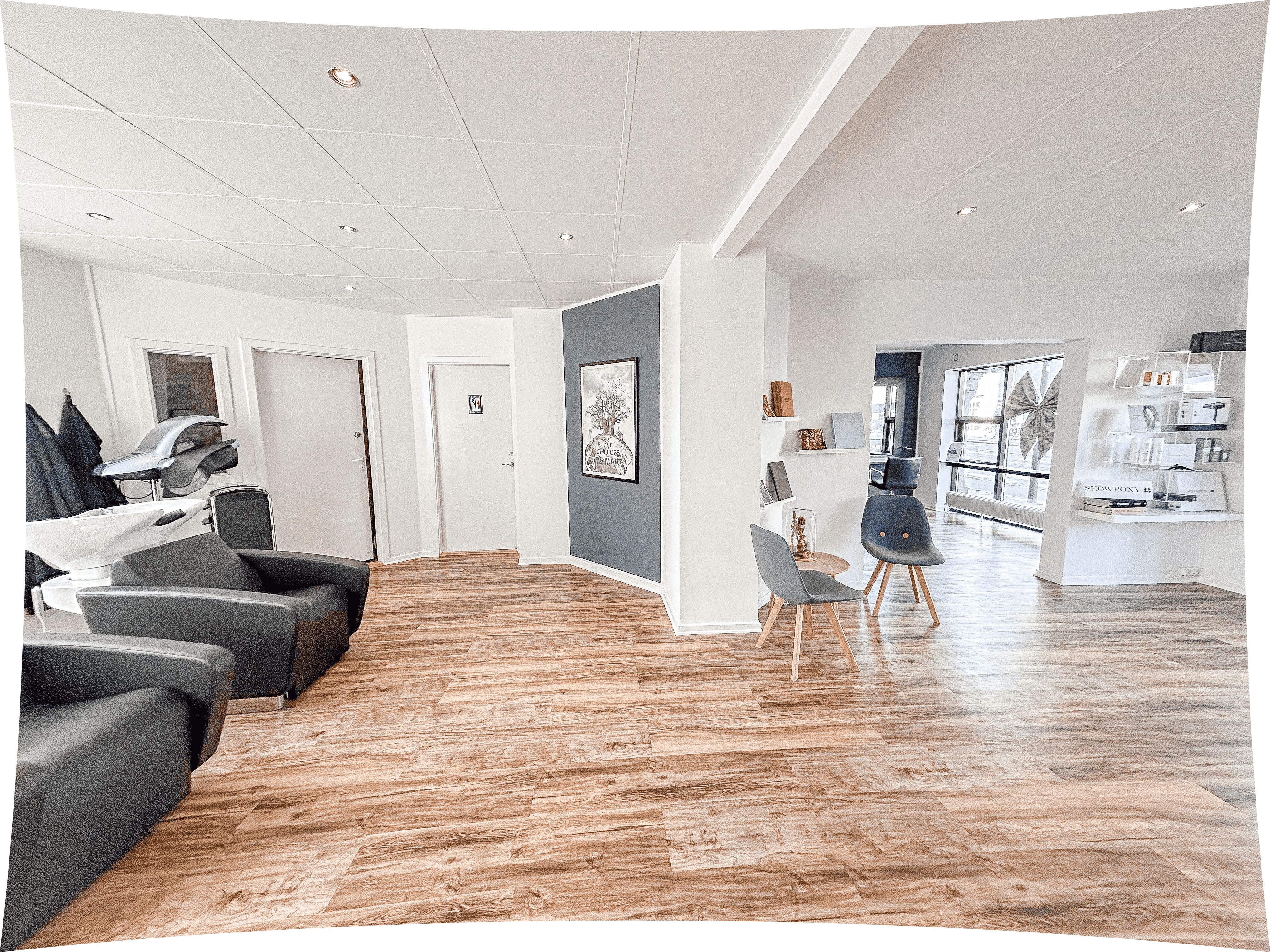 Inde i en stilfuld frisørsalon med højt gulv og pæne stole samt lyse og hvide vægge og lofter. Væggen er blå med et maleri