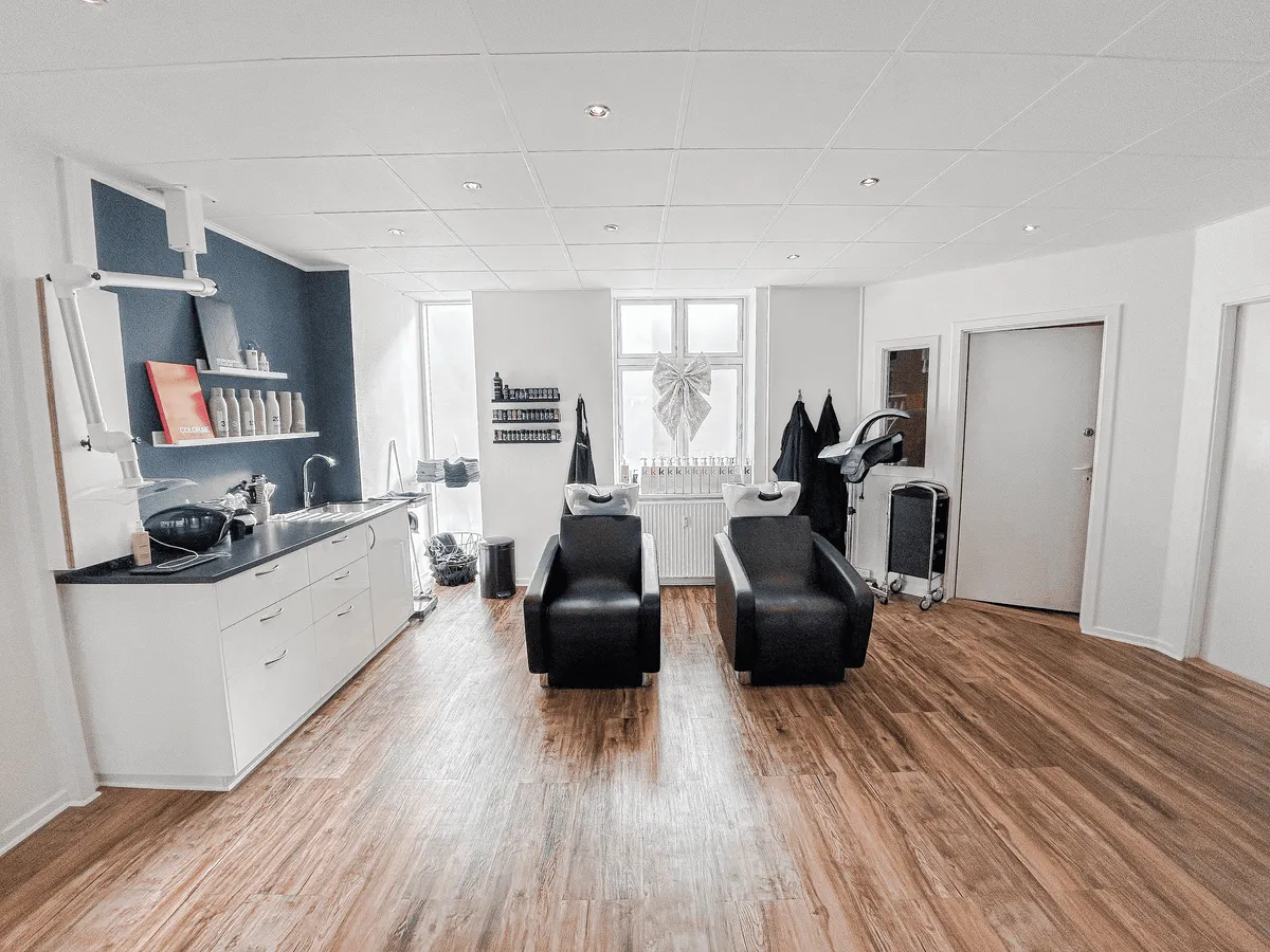 Indvendigt billede af en velplejet frisørsalon med to moderne hårstylingstole, ren, lys og luftig indretning med lysegult