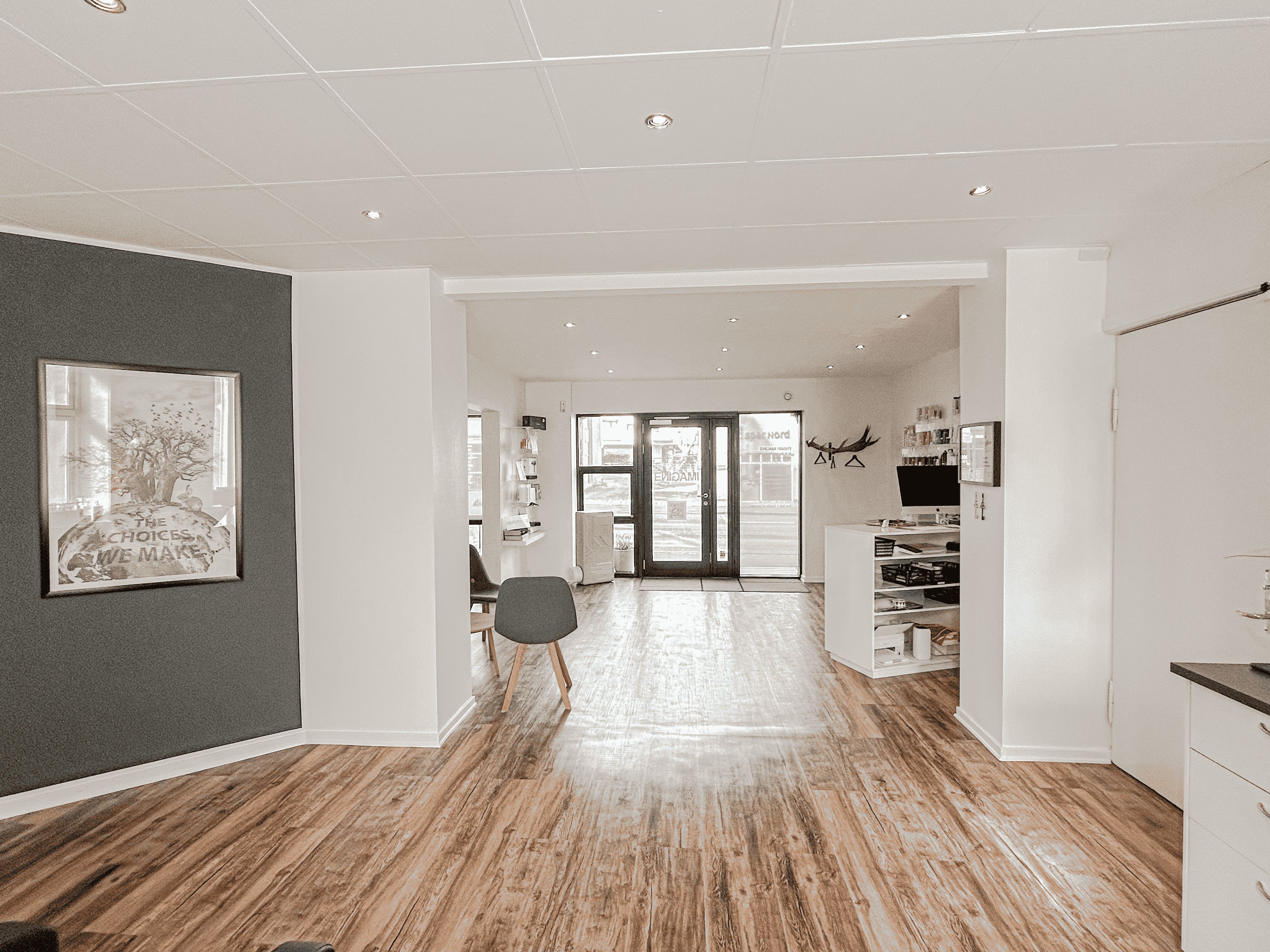 Det er en rummelig og lyse stue med trægulv, åbne døre og et stort maleri på væggen. Der er en sofa og en lampe, og der er