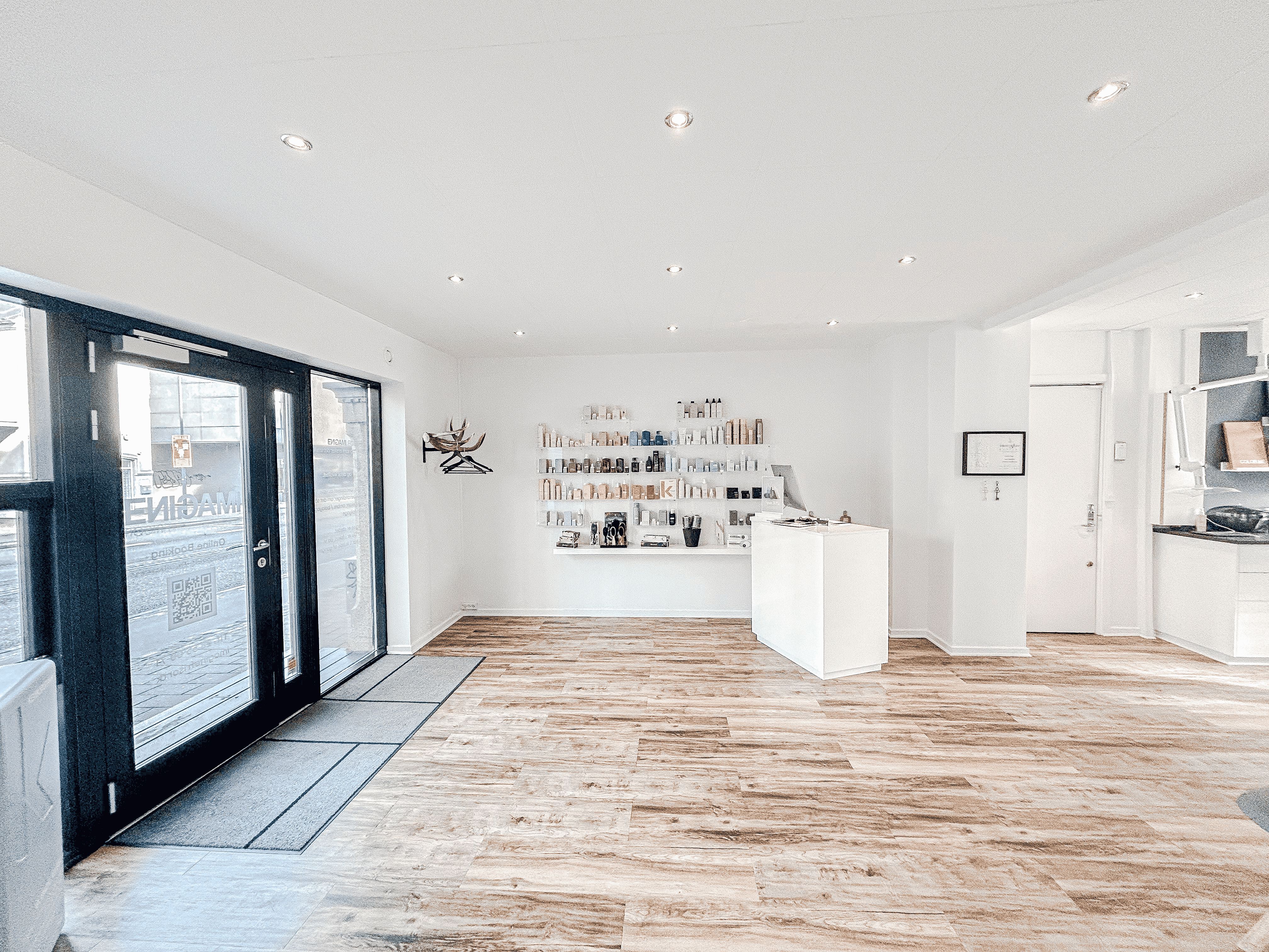 Elegant, hvidt interiør med lysegult gulv og lysepunkter i loftet. Et hjørne med hvide vægge og en hvid reception. Et