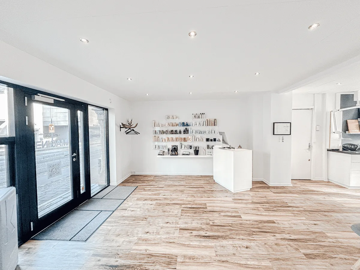 Elegant, hvidt interiør med lysegult gulv og lysepunkter i loftet. Et hjørne med hvide vægge og en hvid reception. Et