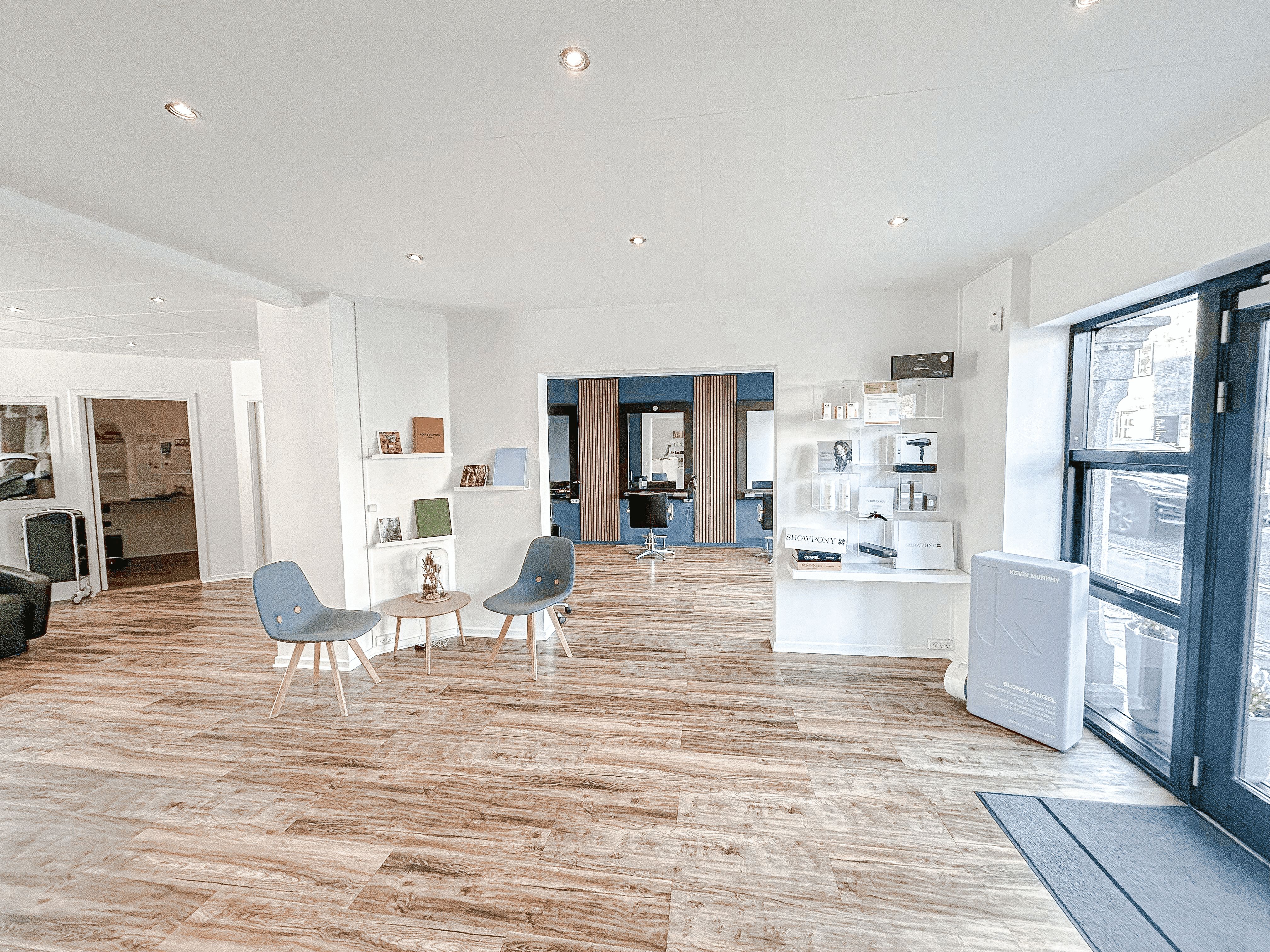 Indvendørs i lyse lokaler med højt til loftet, trægulve og hvide vægge. To lyseblå stole og et lille bord er placeret midt