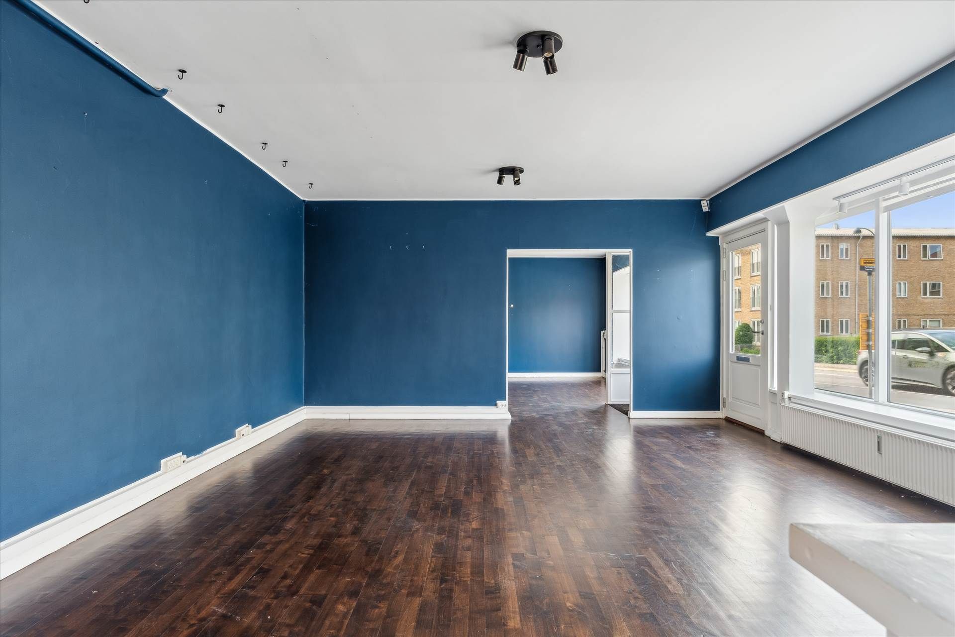 Foto af en tom og nyrenoveret lejlighed med lysegule loft og mørkebrune gulv. Større vinduer og døre med hvide omrammede. I