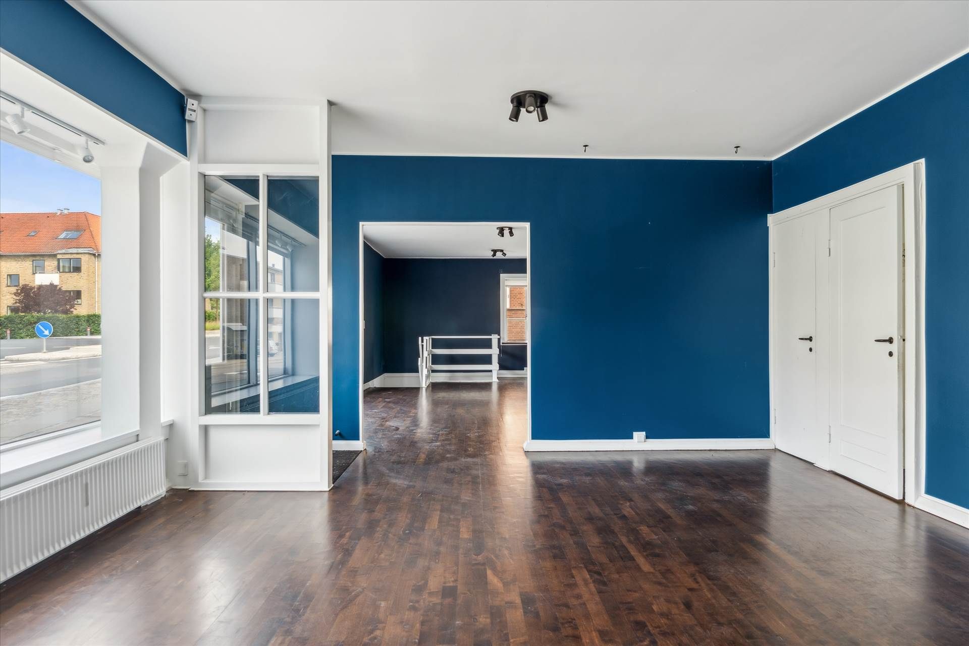 En stor, tom lejlighed med lysegul gulvbelægning, blå vægge, to hvide døre og vinduer med dobbeltruder