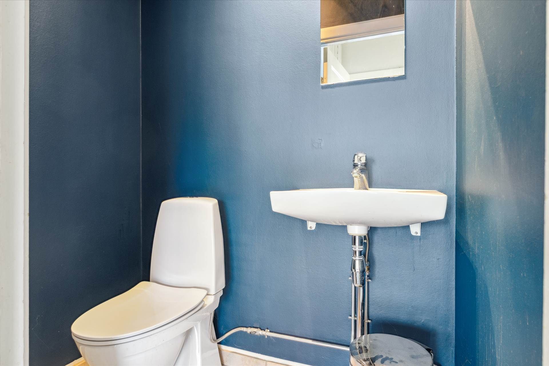 Et lille badeværelse med en hvid toilet og et hvidt vask, der er monteret på den højre side af badeværelset.